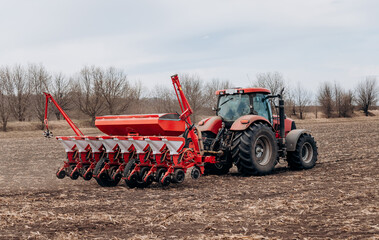 Spring sowing season. Farmer with a tractor sows corn seeds on his field. Planting corn with...