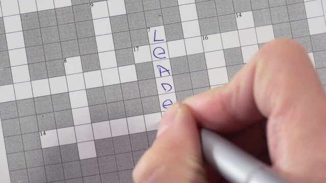 A man solves a crossword puzzle with the words teamwork, leader, trust.