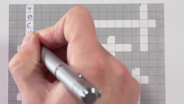 A man writes with a pen solves a crossword puzzle with the words technology, mobile, wireless.