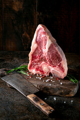 Large raw t-bone steak on a wooden board with seasonings and pepper. Florentine or Porterhouse steak with a meat cleaver