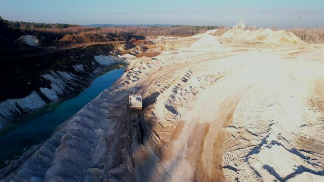 Mining dump truck transporting chalk rock from an open pit. Mining clay in limestone quarry. Anthropogenic landscape with mountains in open cast mine. 
