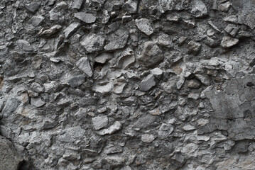Rough dark gray stone wall made of cobblestones and concrete. Texture uneven stone background