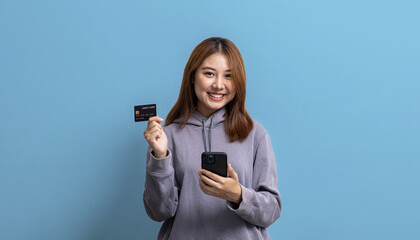Portrait of beautiful Asian woman holding credit card and mobile phone on isolated background,...