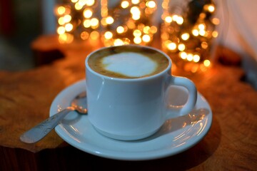 taza de café blanca, disfrutando de un buen late en un día frío sobre una mesa rústica con luces de fondo.