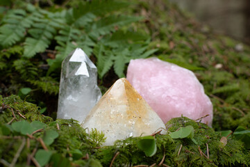 Crystals or raw gemstone minerals on a forest floor with lush greenery. Clear quartz, rose quartz...