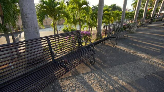 Beautiful metal benches on the background of royal palm trees on the Plaza de la Hispanidad or Spain at sunrise. Popular tourist landmark in Colonial city of Santo Domingo, Dominican Republic. 