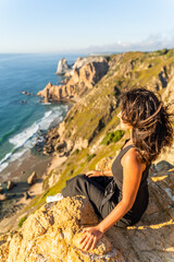 Young Girl in Black Dress Sits on a Cliff at Cabo da Roca, Enjoys Sun and Wind