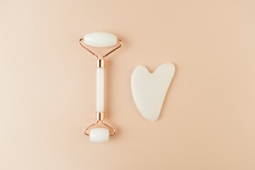 A white Guasha face massager and a face roller lying on a beige background