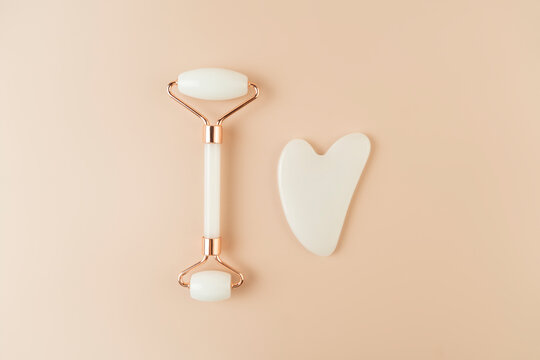 A white Guasha face massager and a face roller lying on a beige background
