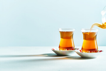 Traditional Turkish black tea pouring from teapot. Fresh tea in glass on saucer on white background with copy space. 