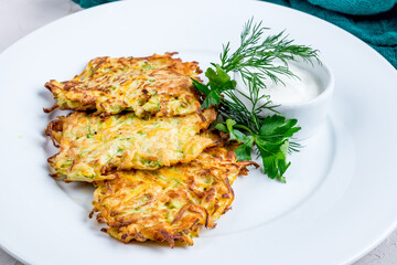 Fried potato pancakes with sour cream on white plate