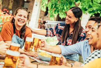 Fototapeta Happy friends clinking beer glasses in brewery pub garden - Young people sitting at bar table eating appetizers and drinking alcohol together - Cheerful family dining outside at summertime obraz