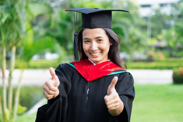 Successful college student in commencement day showing approving thumb up gesture, good education...