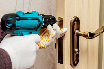 A master with a cordless screwdriver repairs the door lock