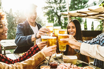 Group of multi ethnic friends having backyard dinner party together - Diverse young people sitting at bar table toasting beer glasses in brewery pub garden - Happy hour, lunch break and youth concept - obrazy, fototapety, plakaty