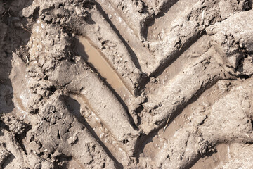 Footprint of wheel tread on the ground road. The trail from the tread of trucks wheels. Car tire tread imprint on sand, background, texture. Footprints rubber tyres from automobile. Close-up.