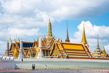 Wat Phra Kaew Temple of the Emerald Buddha, grand palace on the cloudy blue sky day, the most famous spot and must visit place and temple in Bangkok, Thailand including unidentified mask tourist.