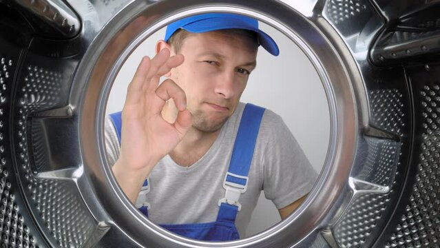 a home appliance washing machine remommer responder looks inside drum of washing machine and points his fingers to gesture or sign all right or okay. Class. Lot of work done. Service men.