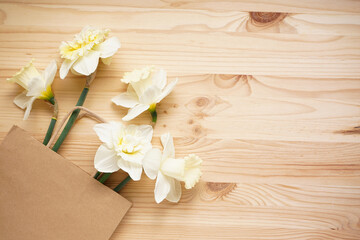 Fototapeta na wymiar Yellow daffodil flowers and paper bag on wooden background with space for text. Top view.