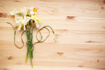 Daffodil flowers with green ribbon on wooden background with space for text. Top view.