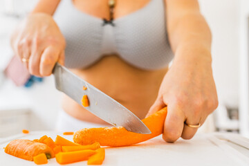unrecognizable woman in lingerie, bikini and bra, with curvaceous figure, cuts fresh carrots with large chef's knife.