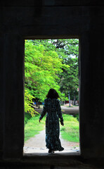 Behind look of woman walking through a gate to a green garden pathway in Angkor Wat, Siem Reap,...