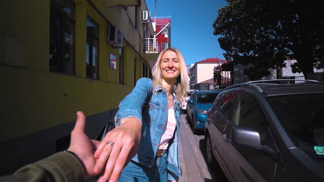 Shooting in first person, young beautiful blonde takes guy by hand and runs along street of old town on sunny day. woman in denim suit, girl. camera follows him. Travel enthusiasts. couple in love.
