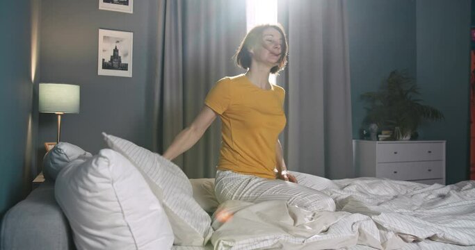 Depressed young caucasian woman sit alone on bed, throwing pillow and pounding fists. Beautiful caucasian female waking up in the morning feel stressed.