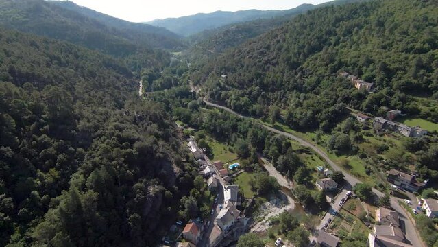 Survol d'une vall&eacute;e montagneuse et bois&eacute;e au-dessus d'un village encaiss&eacute; travers&eacute; par une route dans les c&eacute;vennes du Sud de la France.
