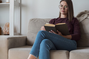 Woman reading book sitting in sofa at home