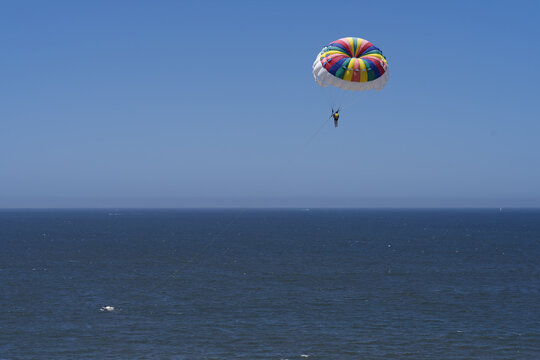 Image of a parasailer in mid air, blue sky and sea, shown in Puerto Vallarta, Mexico.