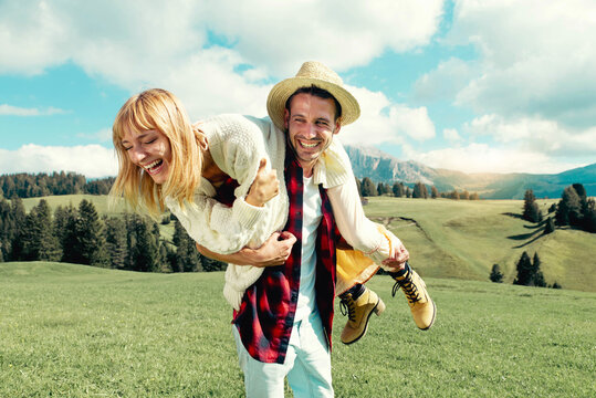 Happy couple enjoying summertime in grass field - Tourists on vacation visiting italian dolomites alps - Two lovers having day trip in the nature