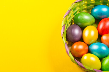 Fototapeta na wymiar Easter colored eggs in a wicker green basket on a yellow background
