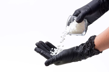 On white background - depilation wax granules in female hands in black gloves.