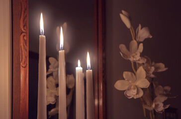 Four lit white taper candles in front of a mirror, candlelight illuminating an orchid plant, nobody