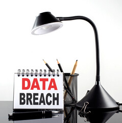 DATA BREACH text on notebook with pen and table lamp on the black background