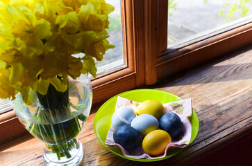 Colored eggs and yellow daffodils on a wooden windowsill