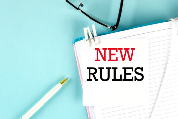 NEW RULES text on a sticky on notebook with pen and glasses , blue background