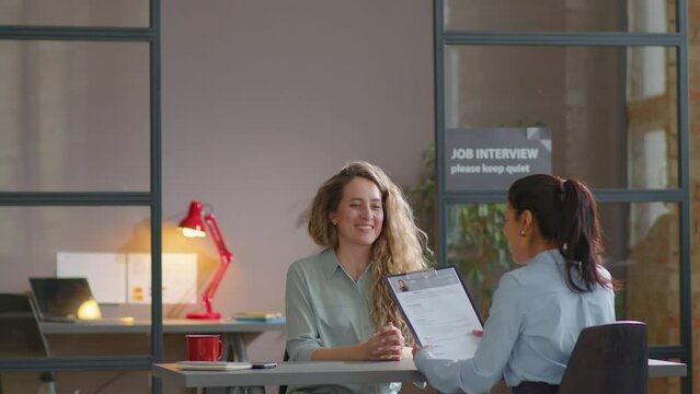 Caucasian businesswoman walking into office, giving CV to recruiter and talking to her during job interview