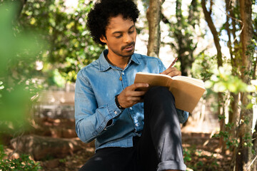 serious man writing in notebook ideas and enjoying nature in wooded area