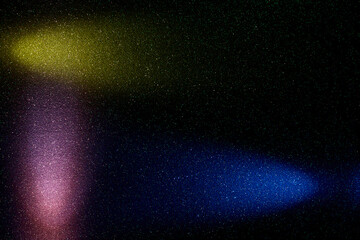 On a black background in fine green grain, rays of blue yellow and gradient pink light