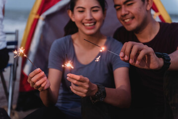While camping, an Asian couple enjoys playing with sparklers fireworks.