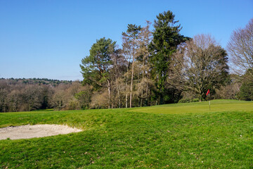 view over parkland golf course. Flag stick and green with bunker of golf course on sunny day. 