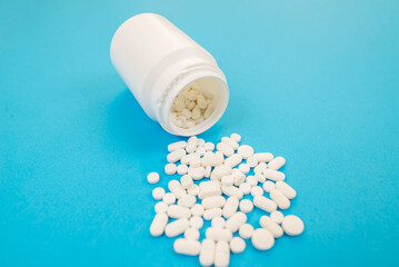 White pills spill out of a plastic bottle. Capsules on a blue background. pharmaceutical industry. Pharmaceutical concept. pharmaceutical products.