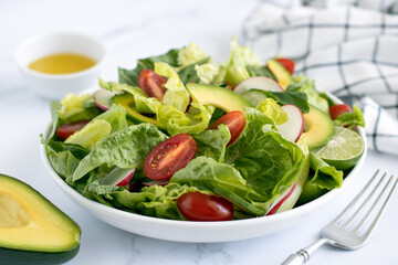 Fresh mix salad of avocado, tomato, cucumber, radish with olive oil on a wooden table, side view.