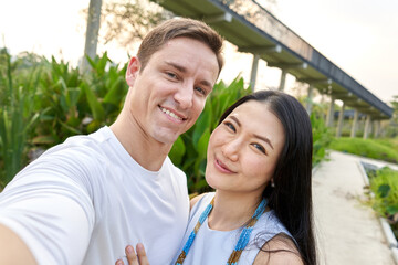 Smiling multiracial couple taking a selfie in a uran park during sunset