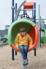 Young boy with Autism wearing a yellow rain coat sits while on playground; joy and play in his own way