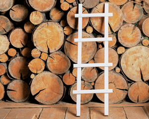 A white ladder with rungs is leaning against a woodpile in the barn. The woodpile made of cross-cut trees is high - obrazy, fototapety, plakaty