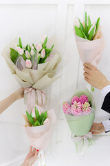 Spring flowers bouquets. Couple man and woman hands holding white and pink tulips and hyacinths mono bouquets.