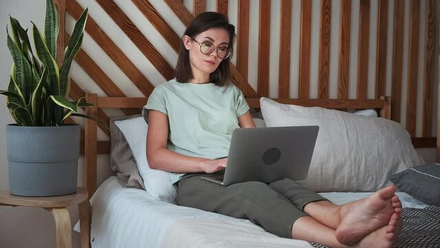 Young woman using laptop, typing, lying on the bed, remote work, work at home